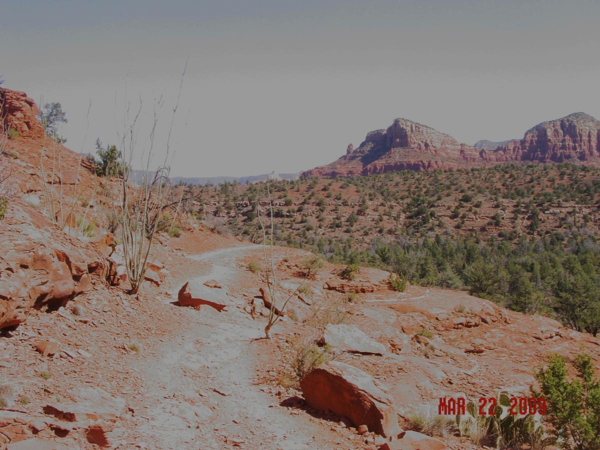 A rocky desert trail winding through red earth and sparse vegetation, with distant red rock formations visible in the background and clear blue skies above. The image is dated March 22, 2009. Templeton mountain bike trail.