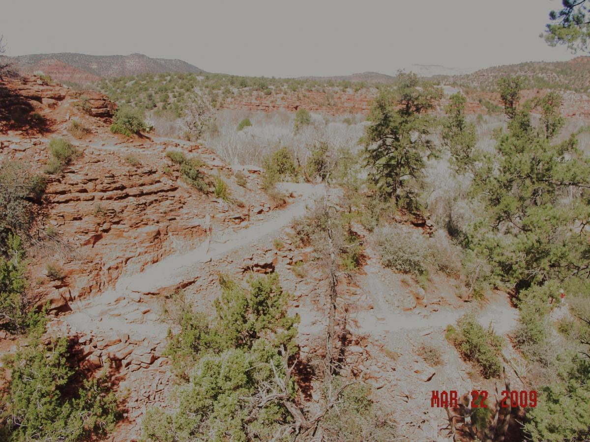 A scenic landscape featuring rocky terrain with reddish-brown cliffs and sparse vegetation. A winding path can be seen, leading through the rugged terrain. In the background, rolling hills and distant mountains are visible under a bright sky. The image is dated March 22, 2009, in the lower right corner. Templeton mountain bike trail.
