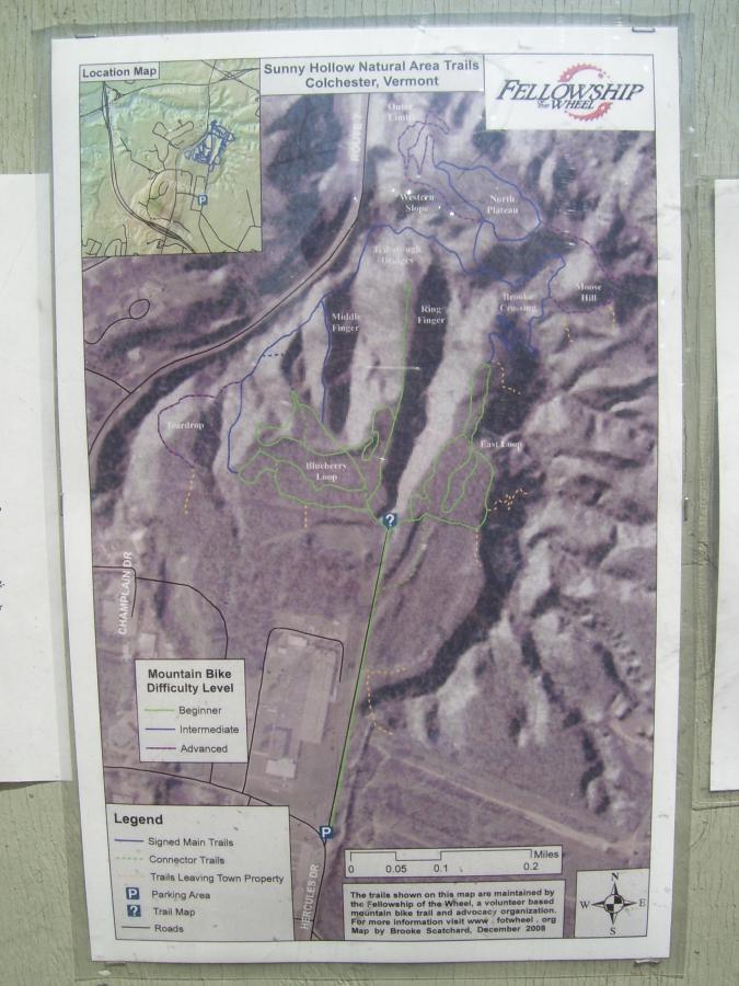 Map of Sunny Hollow Natural Area Trails in Colchester, Vermont, depicting mountain biking trails with difficulty levels indicated. Features include signed main trails, connector trails, and a parking area. The map includes a location inset and a scale for distance measurement. Sunny Hollow mountain bike trail.