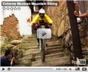 A mountain biker wearing a helmet and a yellow shirt rides down a steep, uneven set of stairs in a historic setting, while a photographer captures the action. The video title is "Extreme Mexican Mountain Biking."