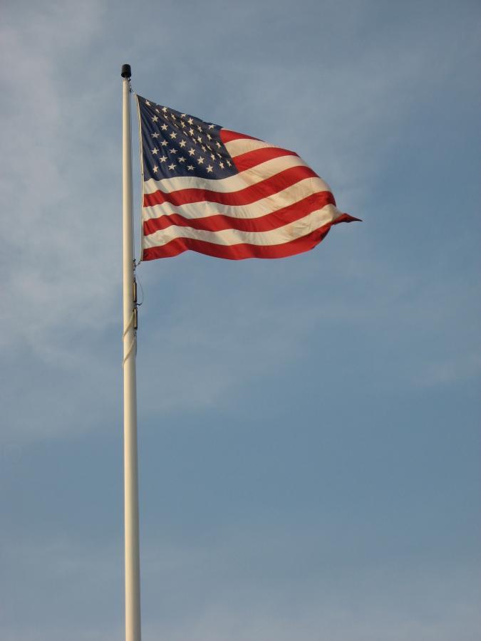 American flag fluttering on a tall flagpole against a clear blue sky. Bluff Trails mountain bike trail.