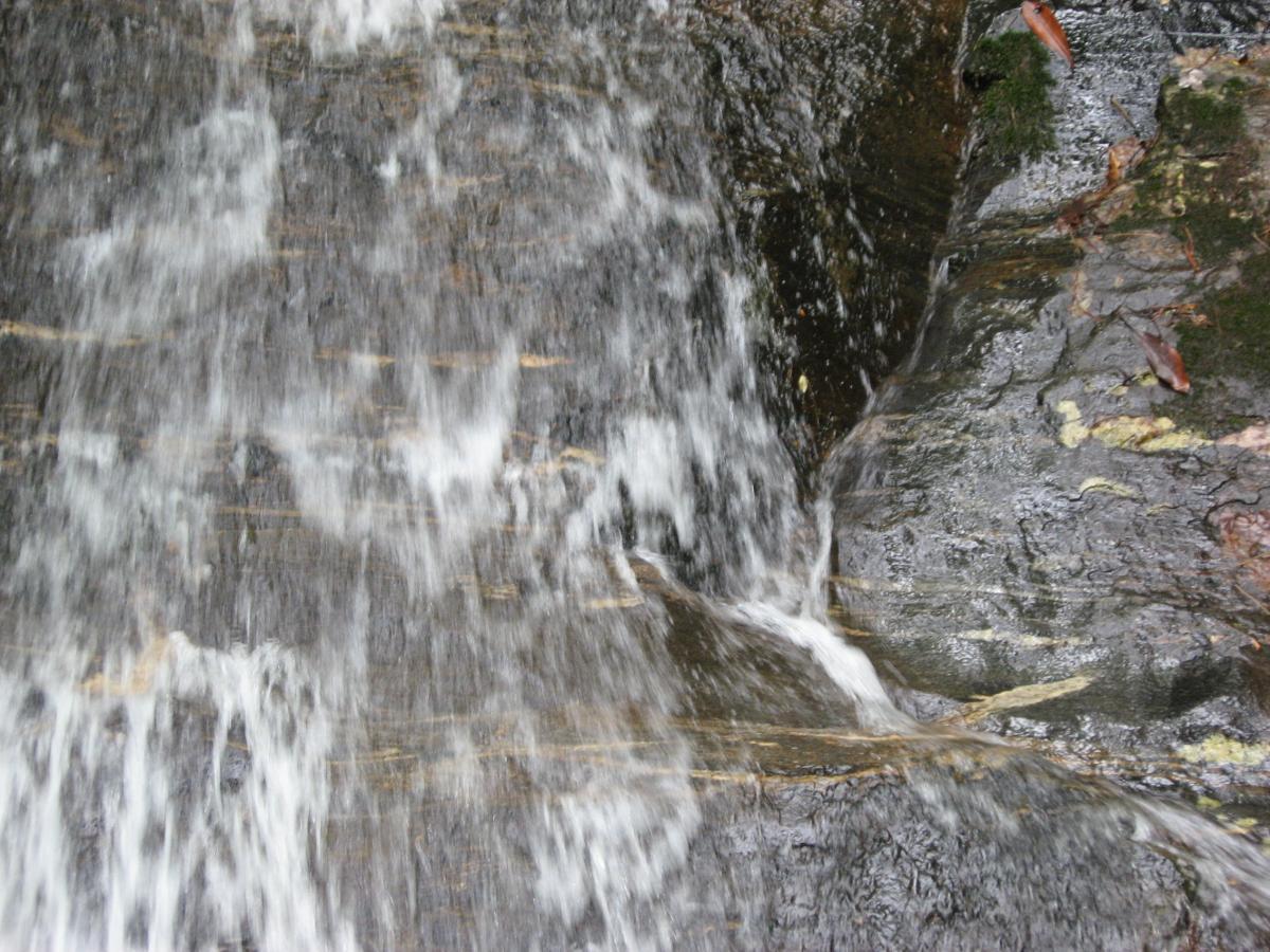 A cascading waterfall flowing over textured rocks, creating a misty spray. Hickory Nut mountain bike trail.