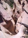 A narrow canyon with layered rock formations in various shades of pink and beige, surrounded by greenery at the top. Mary's Loop / Horsethief Bench mountain bike trail.