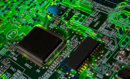 Close-up view of a printed circuit board featuring intricate pathways, small components, and two prominent microchips against a vibrant green background.