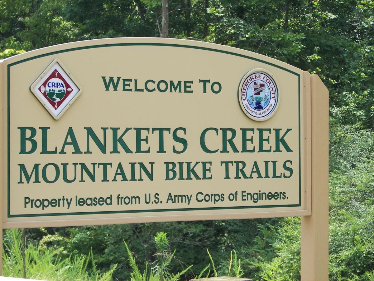 Welcome sign for Blankets Creek Mountain Bike Trails, surrounded by greenery, indicating property leased from the U.S. Army Corps of Engineers. Blankets Creek mountain bike trail.