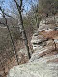 A rocky cliffside with exposed rocks and sparse trees in a natural landscape under a clear blue sky. Raccoon Mountain Trail Network mountain bike trail.