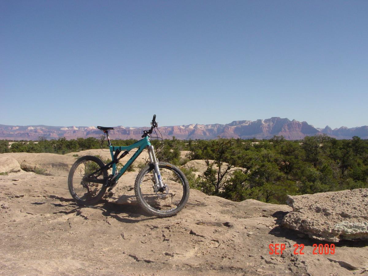 Mountain bike resting on rocky terrain with a panoramic view of distant mountains and clear blue sky in the background. Gooseberry Mesa mountain bike trail.