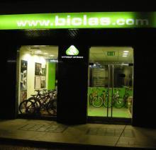Image of a bike shop storefront at night, featuring large glass doors and bright green signage with the website www.biclas.com. Inside, several bicycles are displayed against a green backdrop.