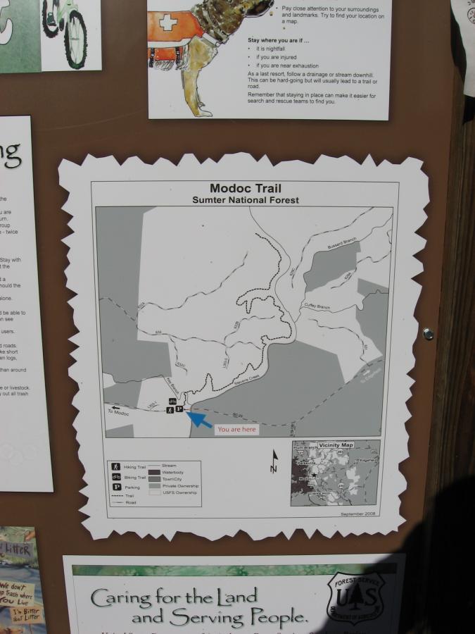 Map of the Modoc Trail in the Sumter National Forest, displaying trail routes, parking areas, and other key features. The map includes a "You are here" marker and is bordered by a decorative scalloped edge. Additional informational text and illustrations are visible in the surrounding area. Modoc (Stevens Creek Trail) mountain bike trail.