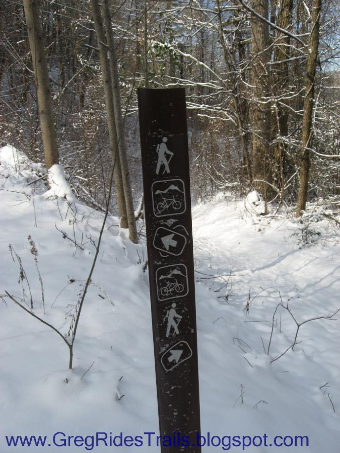 Signpost indicating trail rules and regulations, featuring icons for hiking, biking, and birdwatching, set against a snowy forest background. Fontana Village mountain bike trail.