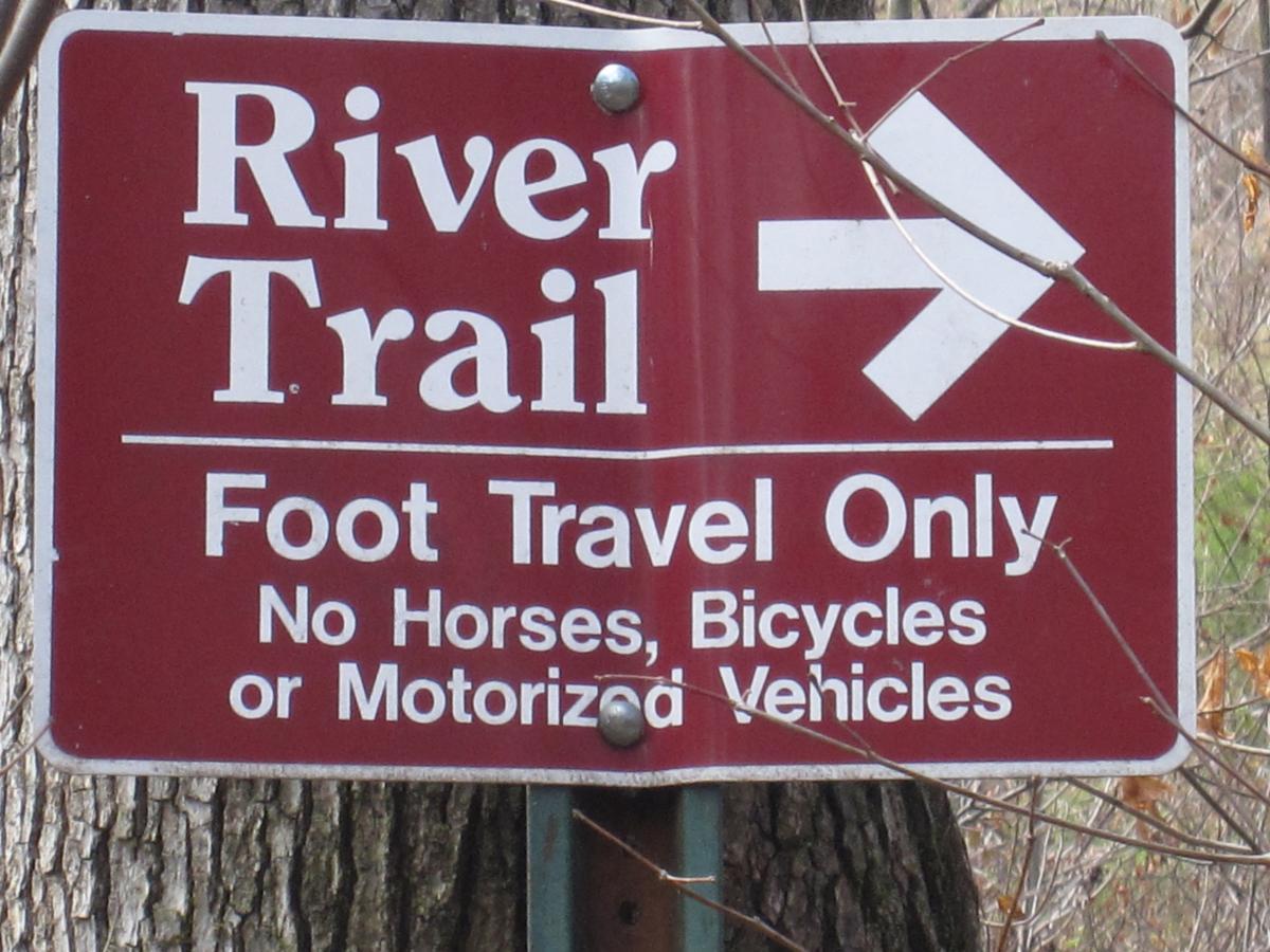 Sign indicating the "River Trail," which is designated for foot travel only. It specifies that horses, bicycles, and motorized vehicles are not permitted. An arrow on the right points toward the direction of the trail. The sign is mounted on a tree. South Rockdale Community Park mountain bike trail.