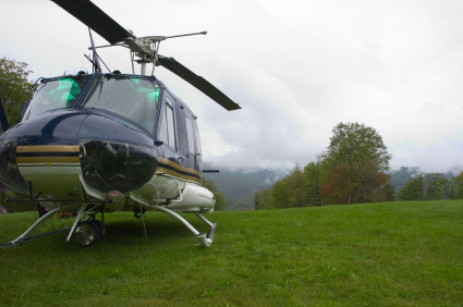 A helicopter is parked on a grassy field with a backdrop of rolling hills and a cloudy sky.