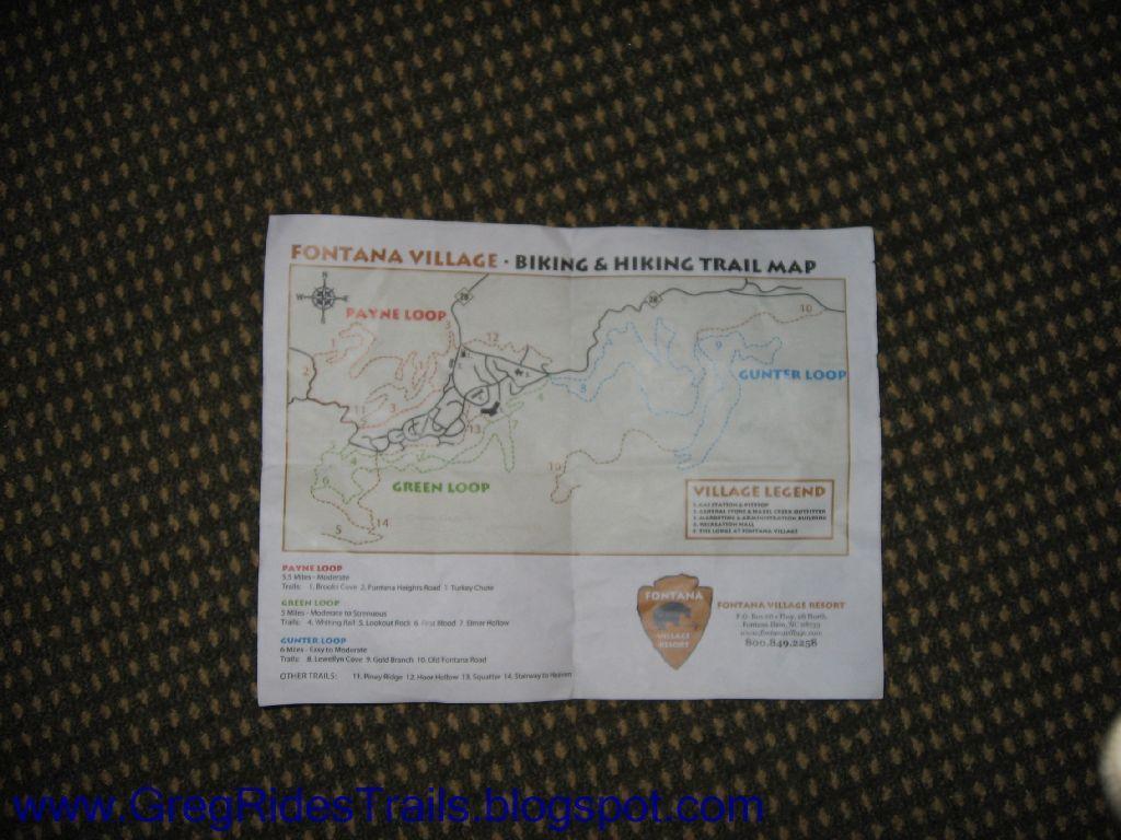 A printed map titled "Fontana Village - Biking & Hiking Trail Map," depicting various trails including the Payne Loop, Green Loop, and Gunter Loop. The map features a legend for trail details and distances, along with a compass rose for orientation. Fontana Village mountain bike trail.
