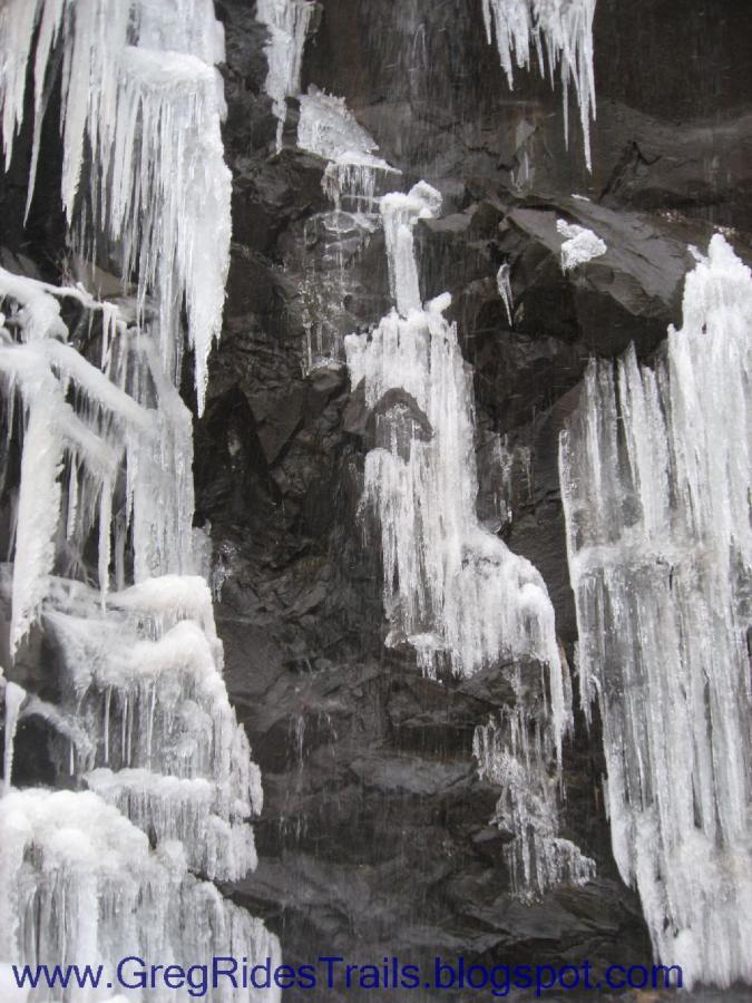 Icicles hanging from a rocky surface, formed by freezing water, creating a striking contrast between the clear ice and the dark rock background. Fontana Village mountain bike trail.