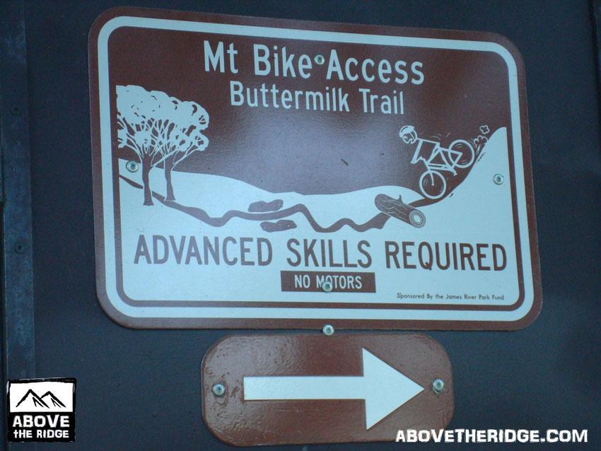Sign indicating access to the Buttermilk Trail for mountain biking, featuring instructions that advanced skills are required and that motorized vehicles are not allowed. The sign includes an image of a cyclist navigating a trail and an arrow pointing to the right for direction guidance. Buttermilk mountain bike trail.
