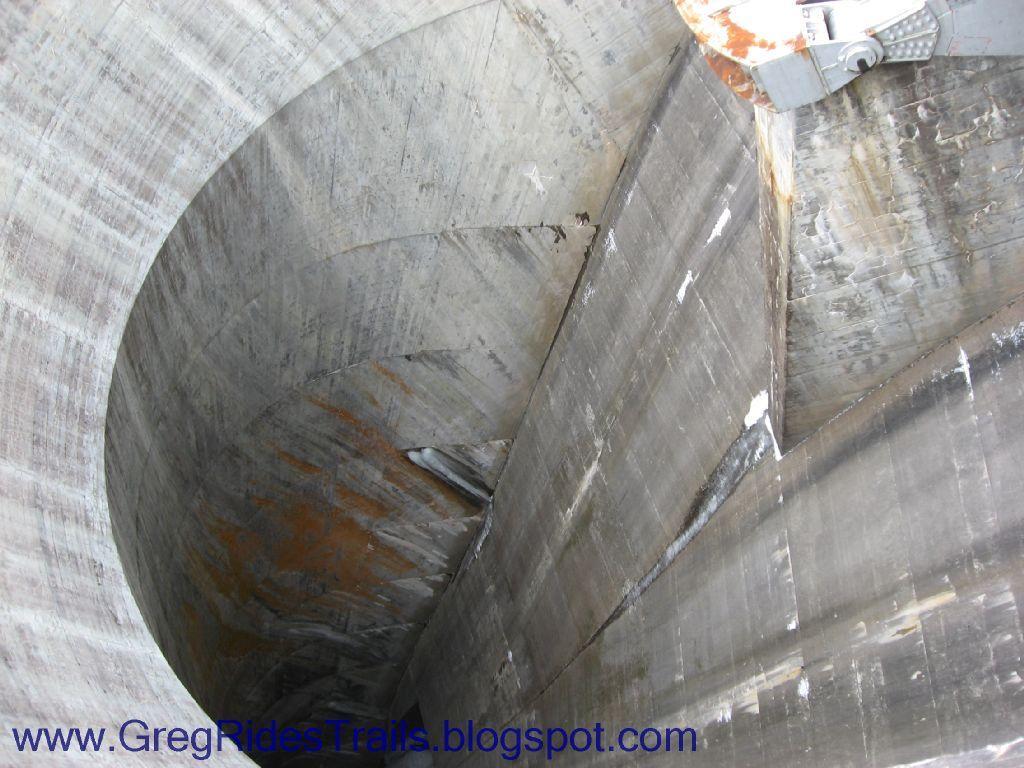Close-up view of a large, concrete cylindrical structure with smooth, curved walls and signs of wear and rust. The image captures the depth and inner surface of the structure, showcasing its industrial design. Fontana Village mountain bike trail.