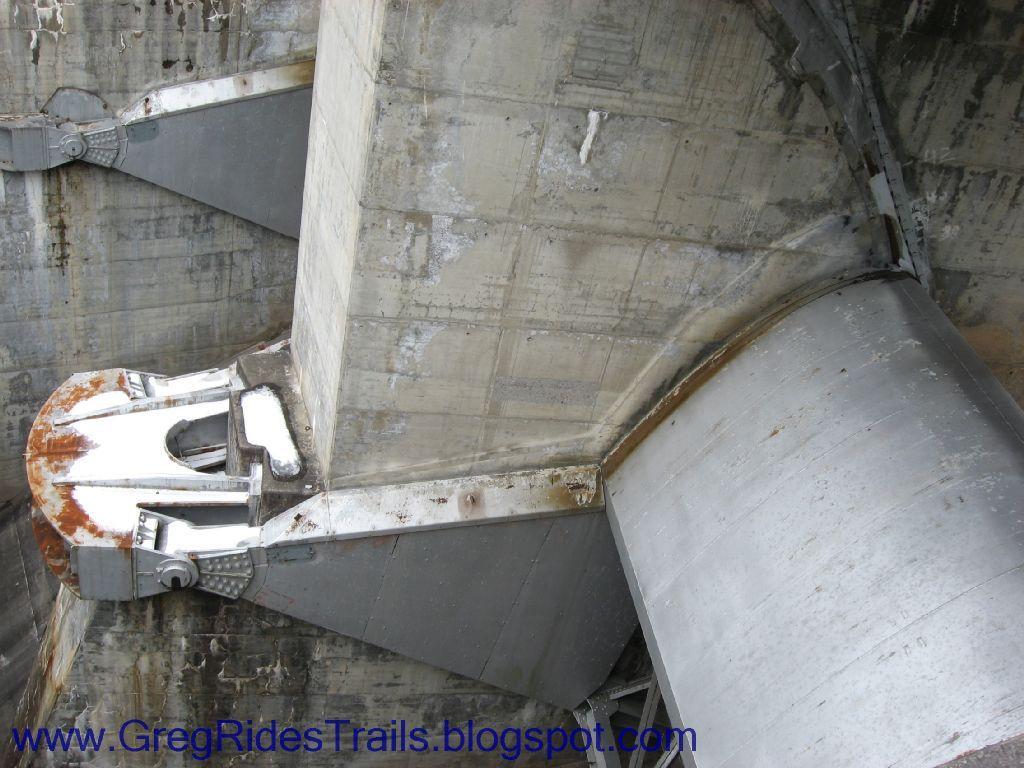 Close-up view of a concrete structure featuring metal components, showcasing industrial design elements and signs of wear, such as rust, with a focus on the mechanisms that support and stabilize the structure. Fontana Village mountain bike trail.