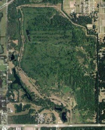 Aerial view of a densely wooded area bordered by a river, with nearby residential and agricultural land. The landscape features green treetops, winding paths, and various clearings, indicating a mix of natural and developed regions. Sydney Dover Trails mountain bike trail.