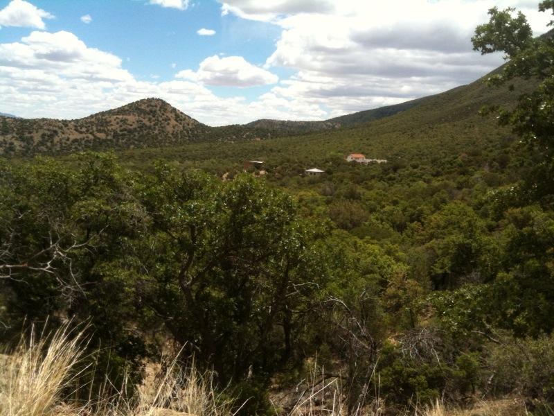 A scenic view of a mountainous landscape featuring rolling hills and a dense wooded area under a partly cloudy sky. In the distance, a few buildings are nestled among the trees, creating a tranquil, natural setting. Brown Canyon mountain bike trail.