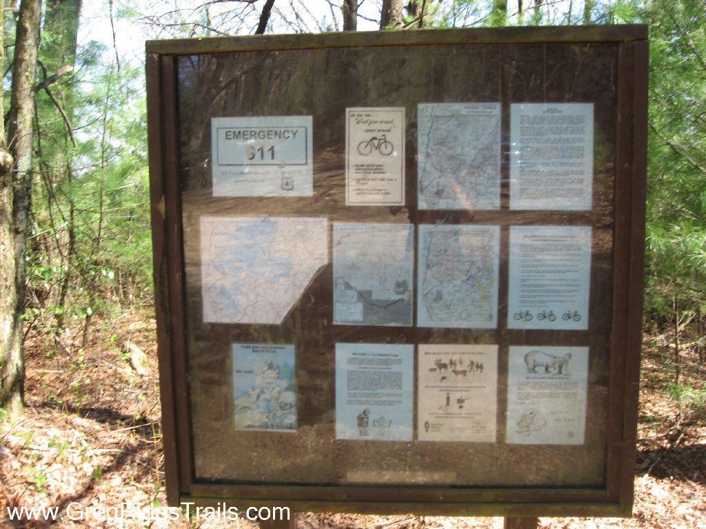 Information board in a forested area displaying maps and guidelines for biking trails, with an emergency contact notice. Bear Creek mountain bike trail.