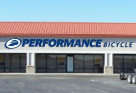 Front view of a retail store featuring a large sign that reads "PERFORMANCE BICYCLE" in bold blue letters, with a red roof and large glass windows.