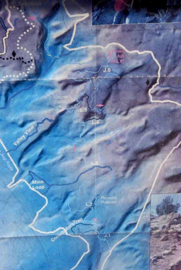 A detailed trail map showing various routes and locations in a mountainous area, including trails labeled with letters and numbers (e.g., J.6, L.5, L.2), and features such as "Valley View," "Mine Loop," and "Parriott's Potholes." The map uses different shades of blue to indicate elevation and terrain, with arrows pointing to specific trails and a legend for guidance. Sovereign Single Track mountain bike trail.