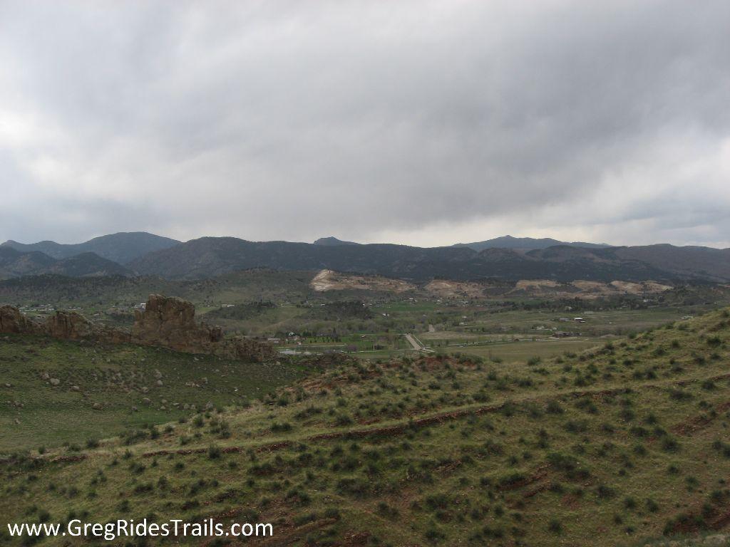 A scenic view of rolling hills and mountains under a cloudy sky, with green grass and rocky outcrops in the foreground, showcasing a tranquil natural landscape. Devil's Backbone mountain bike trail.