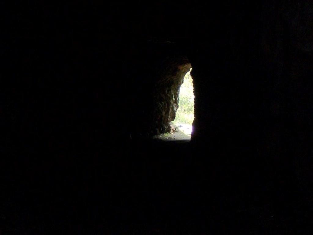 Alt text: A view of light coming from an opening in a dark cave or tunnel, highlighting the contrast between the dark interior and the bright outdoor area. Greenbrier River Trail mountain bike trail.