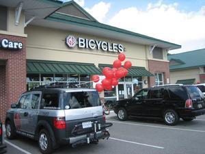 A storefront displaying the sign "Bicycles" with two parked vehicles in front. One vehicle is adorned with red balloons, creating a festive atmosphere.