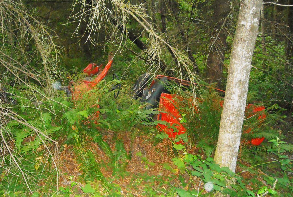 An orange vehicle partially obscured by dense green foliage and trees in a forested area. Lake Sawyer mountain bike trail.