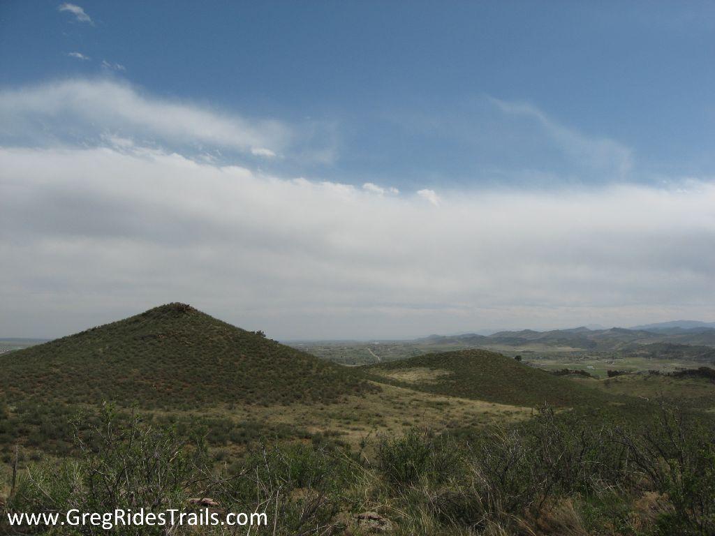 Landscape view of rolling hills and sparse vegetation under a cloudy sky, with distant mountains visible on the horizon. Devil's Backbone mountain bike trail.