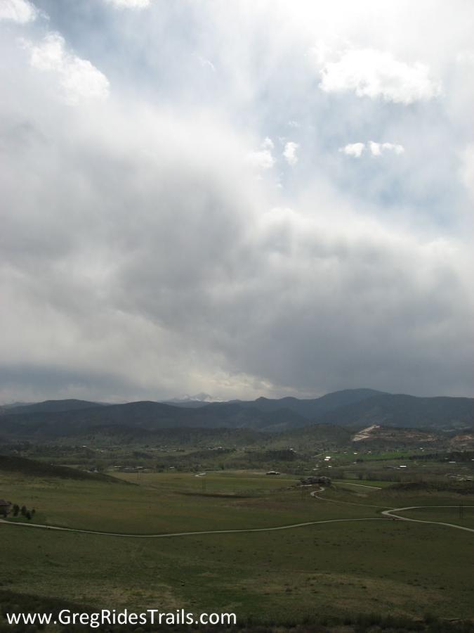 Scenic landscape featuring rolling green hills under a partly cloudy sky, with distant mountains and a winding road. The atmosphere conveys a serene, natural environment. Devil's Backbone mountain bike trail.