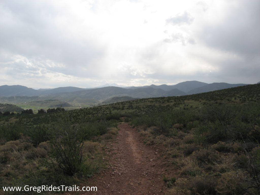 A dirt trail winding through a landscape of rolling hills and sparse vegetation, under a cloudy sky. The scene captures the natural beauty of a mountainous area, inviting outdoor exploration and adventure. Devil's Backbone mountain bike trail.