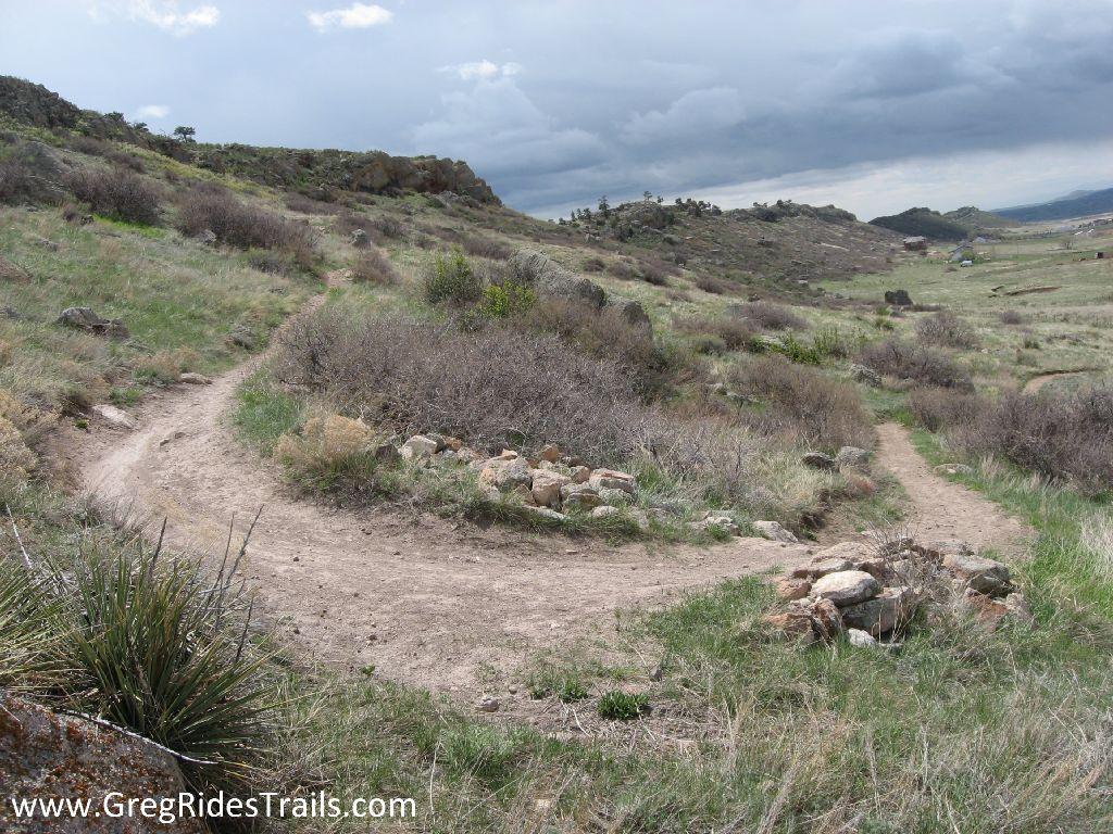 A scenic view of a winding dirt trail surrounded by grassy vegetation and rocky terrain under a cloudy sky. The path curves through the landscape, inviting exploration of the natural setting. Coyote Ridge mountain bike trail.