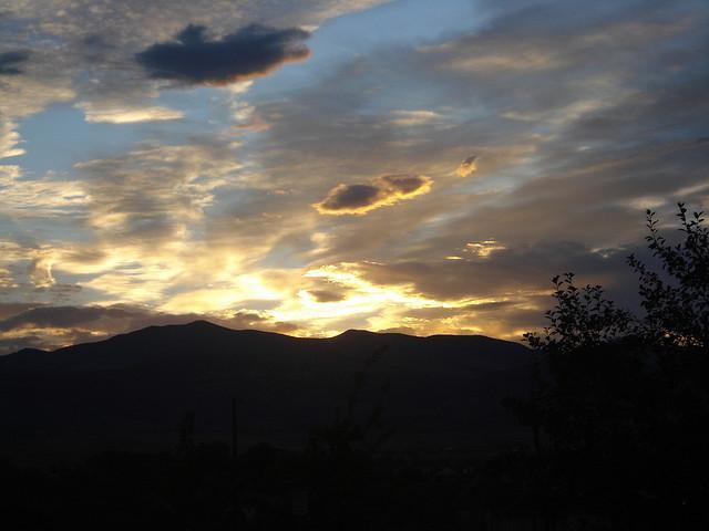 A picturesque sunset over silhouetted mountains, with vibrant colors illuminating the clouds against a blue sky. The scene captures the tranquil beauty of dusk, with hints of orange and yellow blending into the darker shades of the horizon. White Ranch mountain bike trail.
