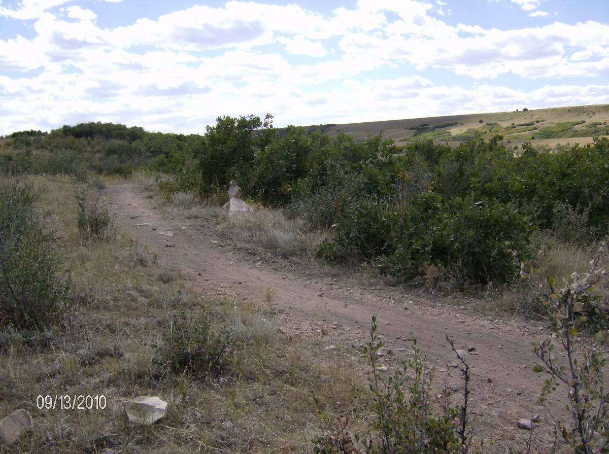 A dirt path curving through a grassy landscape with scattered rocks and shrubs, under a partly cloudy sky. The image captures a serene natural setting, with a gentle slope in the background. The date at the bottom indicates it was taken on September 13, 2010. Ridgeline Open Space Trail mountain bike trail.