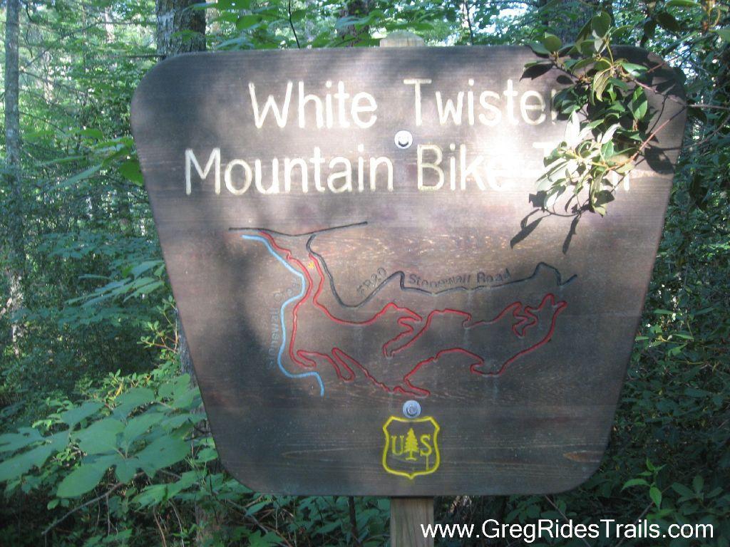 Sign marking the White Twister Mountain Bike Trail, featuring a trail map and the U.S. Forest Service logo, surrounded by greenery in a wooded area. White Twister mountain bike trail.