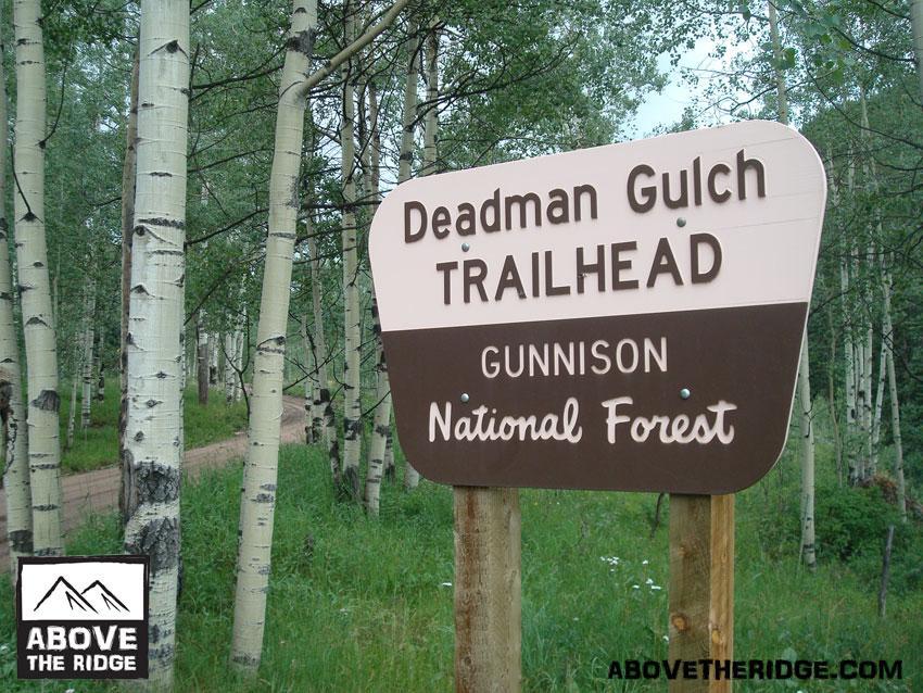 Sign at the Deadman Gulch Trailhead located in Gunnison National Forest, surrounded by aspen trees and a dirt path. Reno / Flag / Bear / Deadman Loop mountain bike trail.