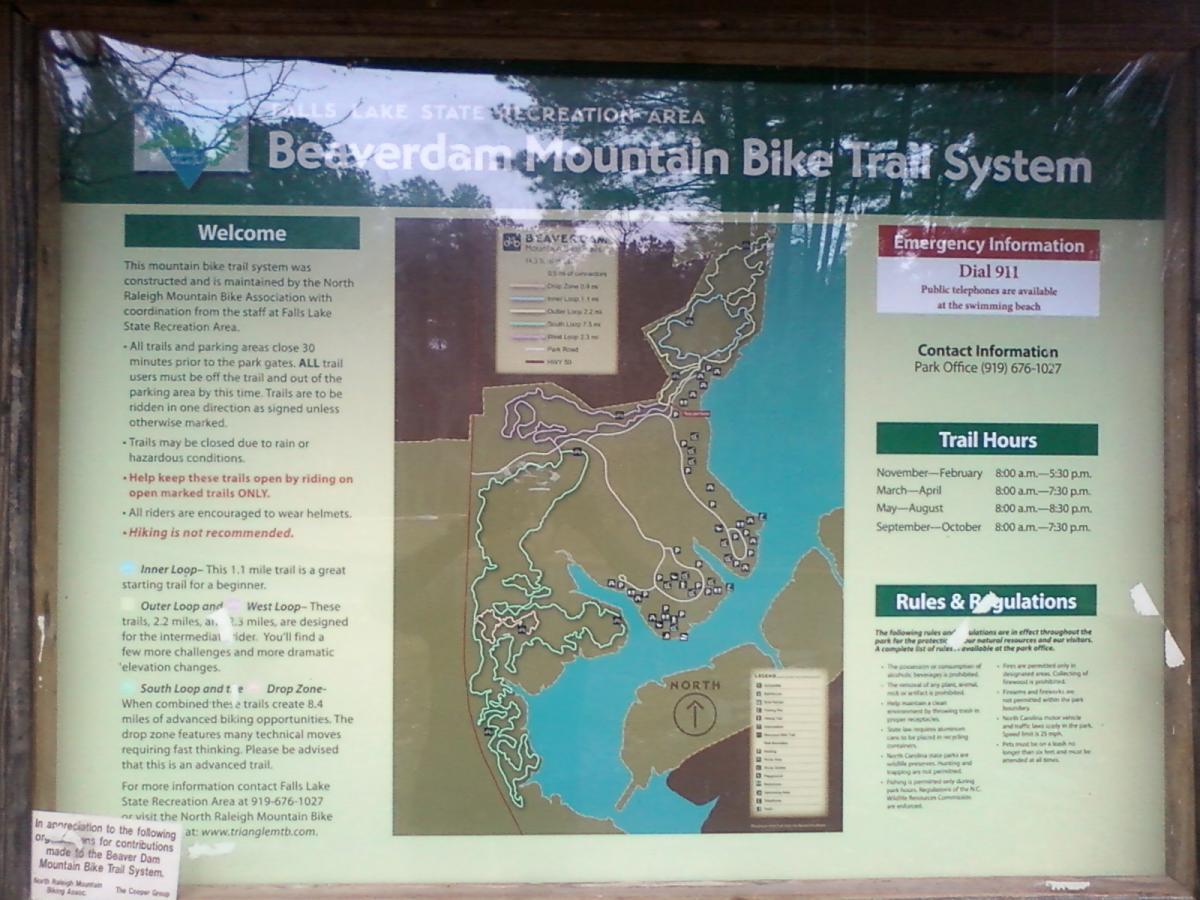 Map and informational sign for the Beaverdam Mountain Bike Trail System located at Falls Lake State Recreation Area. The sign includes details about trail usage, safety recommendations, contact information, operating hours, and rules and regulations for visitors. A trail map illustrates the layout and various loops available for biking, with additional notes on trail conditions and maintenance. Beaver Dam mountain bike trail.