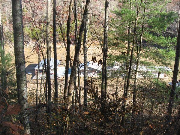 A view through trees overlooking a clearing, where several structures with blue roofs are visible on the ground. The surrounding area features a mix of tall trees and bare branches, indicating it is likely autumn. Tsali Thompson Loop mountain bike trail.