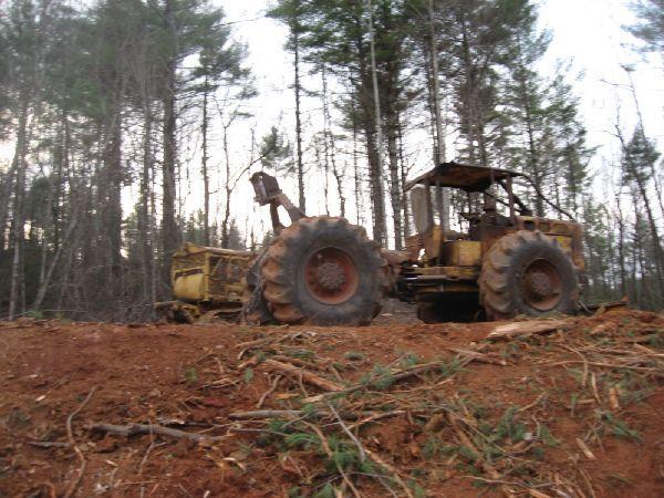 A large, rusty piece of heavy machinery in a forested area, partially obscured by timber debris. The background features tall trees, indicating a wooded environment, with the ground showing signs of recent clearing or logging activity. Montgomery Creek Trail mountain bike trail.