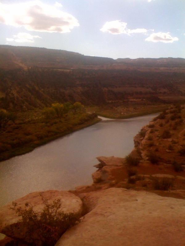 A scenic view of a river winding through a canyon, surrounded by rocky cliffs and sparse vegetation under a partly cloudy sky. Mary's Loop / Horsethief Bench mountain bike trail.