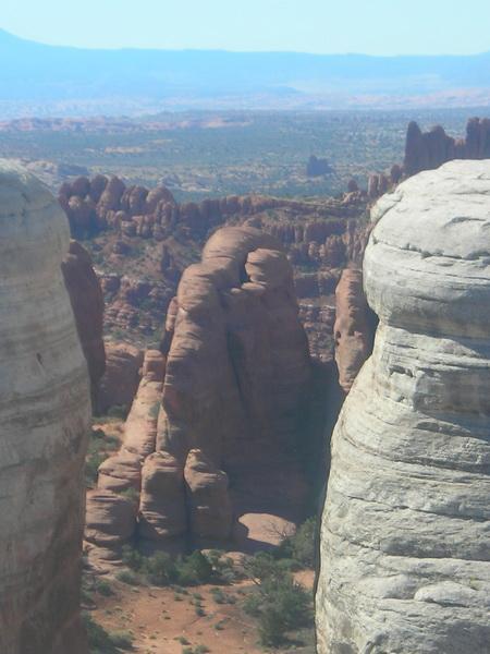 A panoramic view of rugged red rock formations in a desert landscape, showcasing towering cliffs and unique rock shapes under a clear blue sky. Klondike Bluffs mountain bike trail.