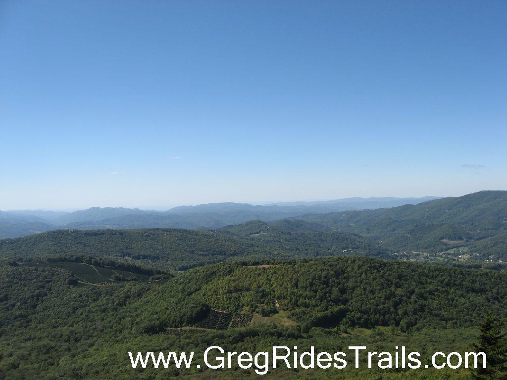 Alt text: "Scenic view of rolling green hills and distant mountains under a clear blue sky." Sugar Mountain Resort mountain bike trail.