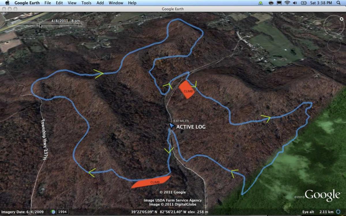 An aerial view from Google Earth showing a topographical map of a hilly wooded area. The map includes marked paths labeled "CLIMB," an "ACTIVE LOG," and various directional arrows indicating routes. The image features terrain with varying elevations and some nearby developed land, with a date stamp of April 8, 2011. Great Seal State Park mountain bike trail.