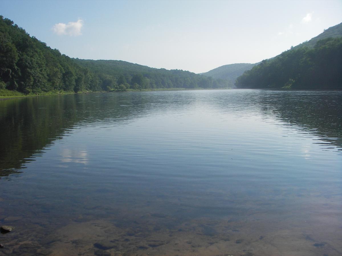Calm river reflecting the surrounding green hills under a clear blue sky, with gentle ripples on the water’s surface. Kennerdell mountain bike trail.