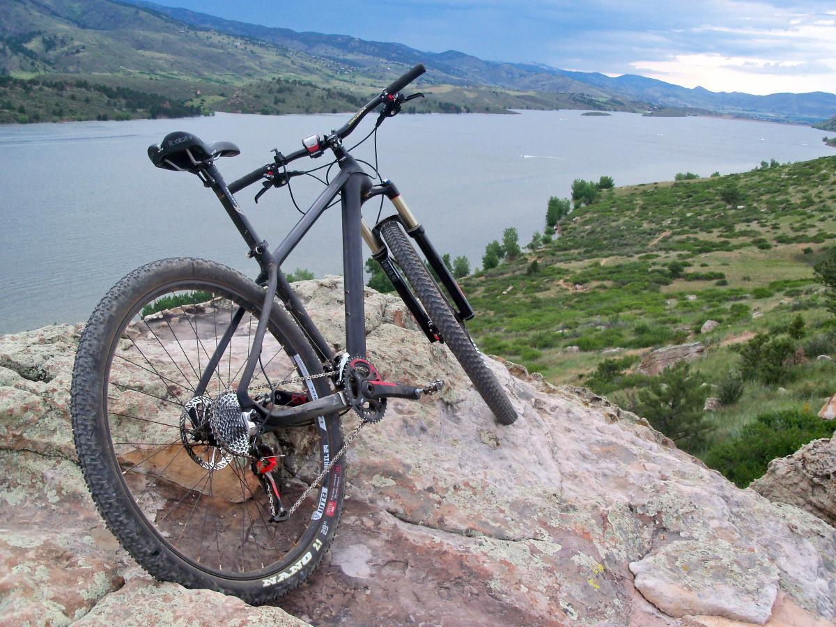 Mountain bike resting on rocky terrain overlooking a lake and rolling hills under a cloudy sky. Foothills Trail mountain bike trail.