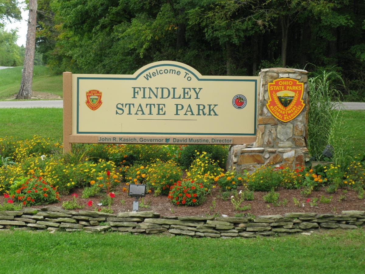 "Welcome sign for Findley State Park, set in a landscaped area with colorful flowers and greenery. The sign features the park's name and logos, along with the names of state officials." Findley State Park mountain bike trail.