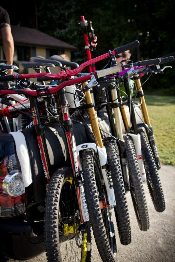 Bikes mounted on a vehicle, showcasing a variety of colorful handlebars and front forks, with a focus on the handlebars' grips and distinctive color patterns against a natural background. Seven Springs mountain bike trail.
