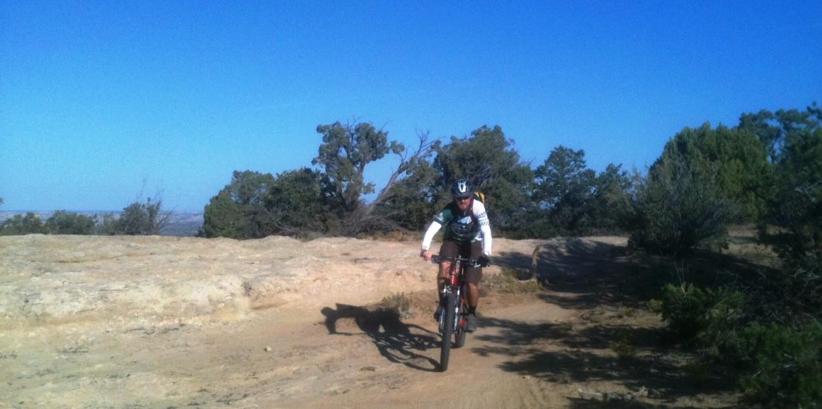 A mountain biker rides along a rocky trail surrounded by sparse vegetation under a clear blue sky. Alien Run Trail mountain bike trail.